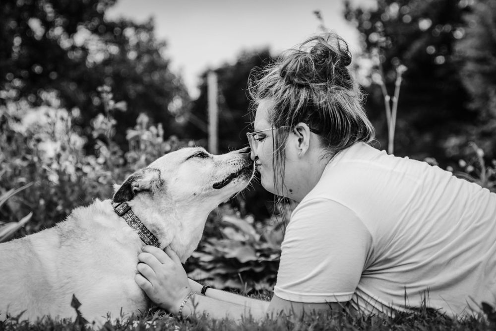 Black and white photo of playful moment between person and white dog outdoors.