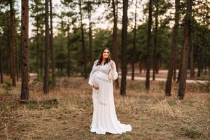 A person in a flowing white lace dress poses gracefully in a pine forest during golden hour.