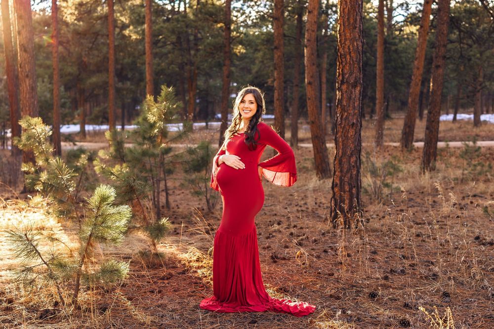 A person in a flowing red dress walks through a sunlit pine forest during golden hour.