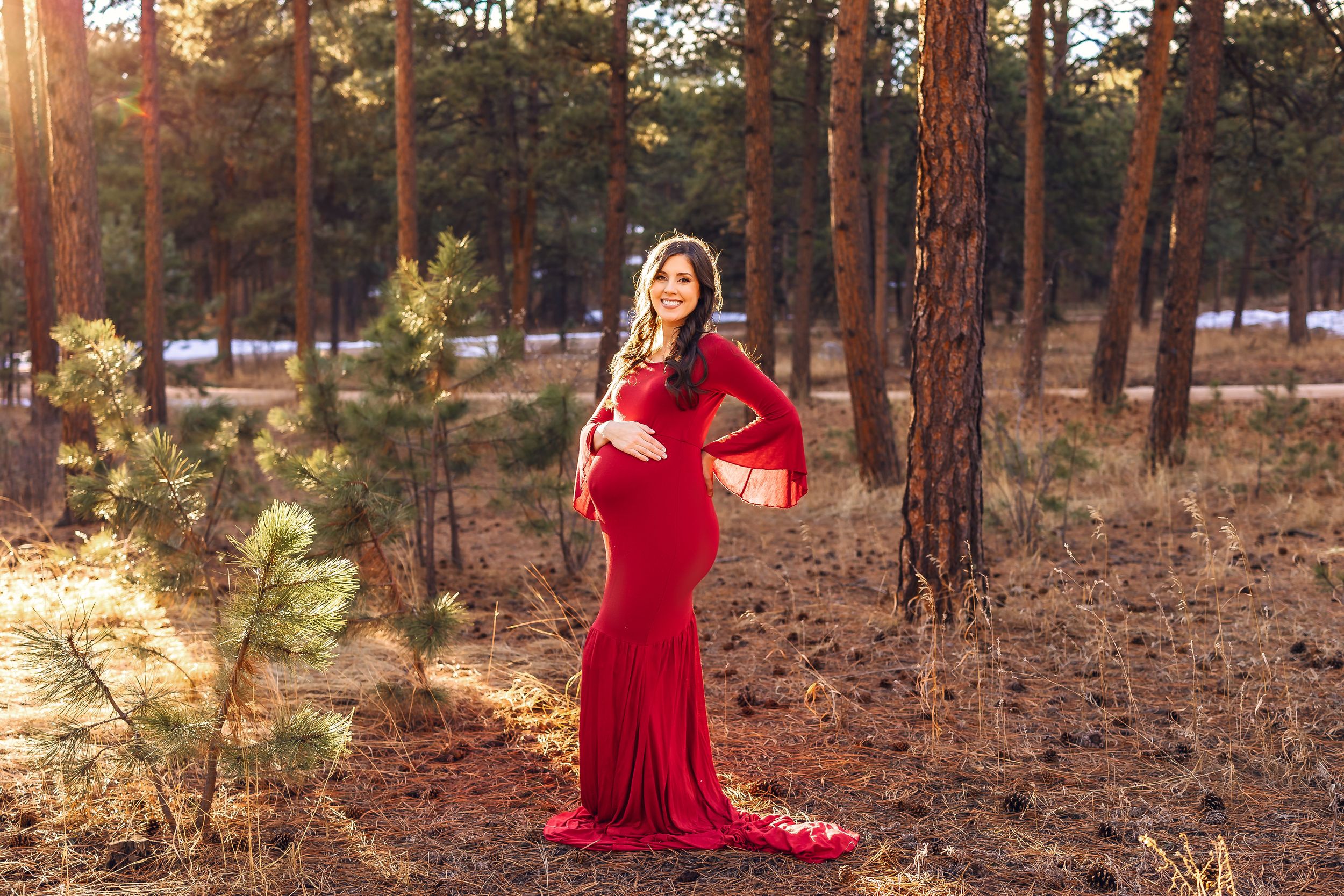 A person in a flowing red dress walks through a sunlit pine forest during golden hour.