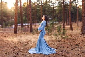 A figure in a flowing light blue dress twirls gracefully among tall pine trees during golden hour.