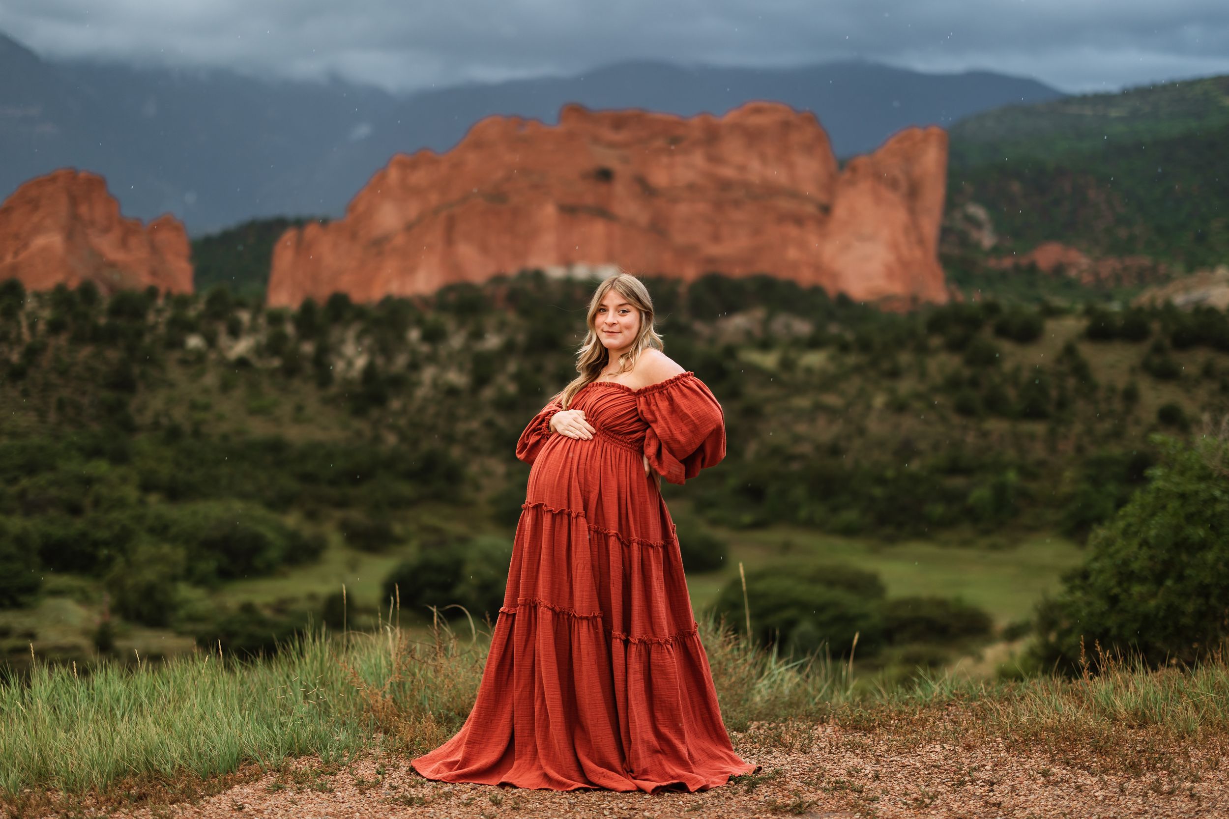 Red-clad figures stand against dramatic rock formations at Garden of the Gods in Colorado during overcast weather.