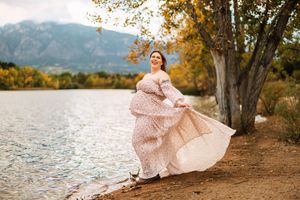 A flowing pink polka dot dress twirls gracefully by a serene lake with autumn trees and mountains in the background.