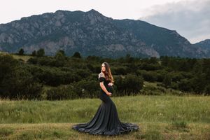 A flowing black dress creates a dramatic silhouette against a mountain landscape during a golden hour photoshoot.