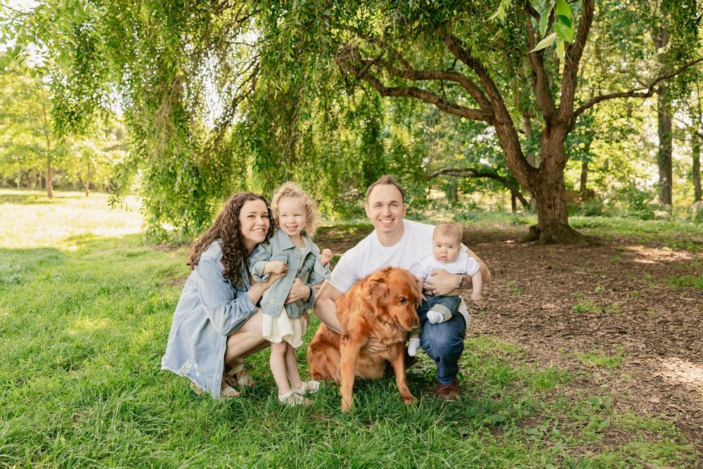 Family and their golden retriever dog pose together under a large tree in a park.