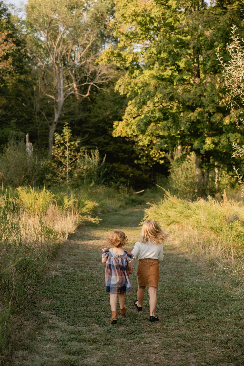 Two figures walk hand in hand down a grassy path surrounded by autumn trees with golden leaves.