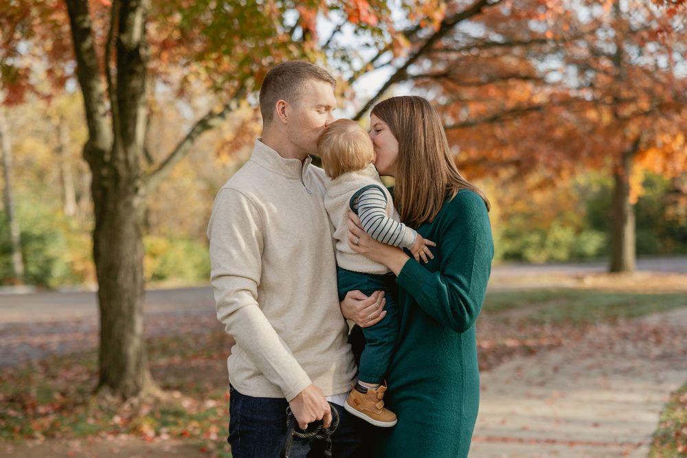 A couple shares tender moments in a park during autumn with golden leaves falling from trees in the background.