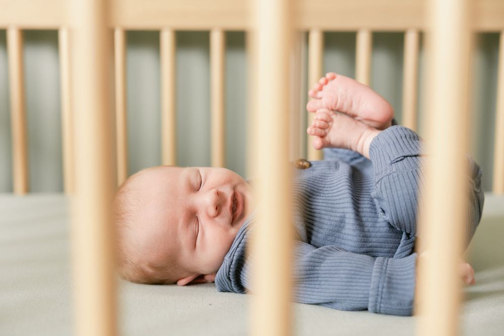 Baby's tiny feet peek through white wooden crib slats while wearing cozy blue striped pajamas.