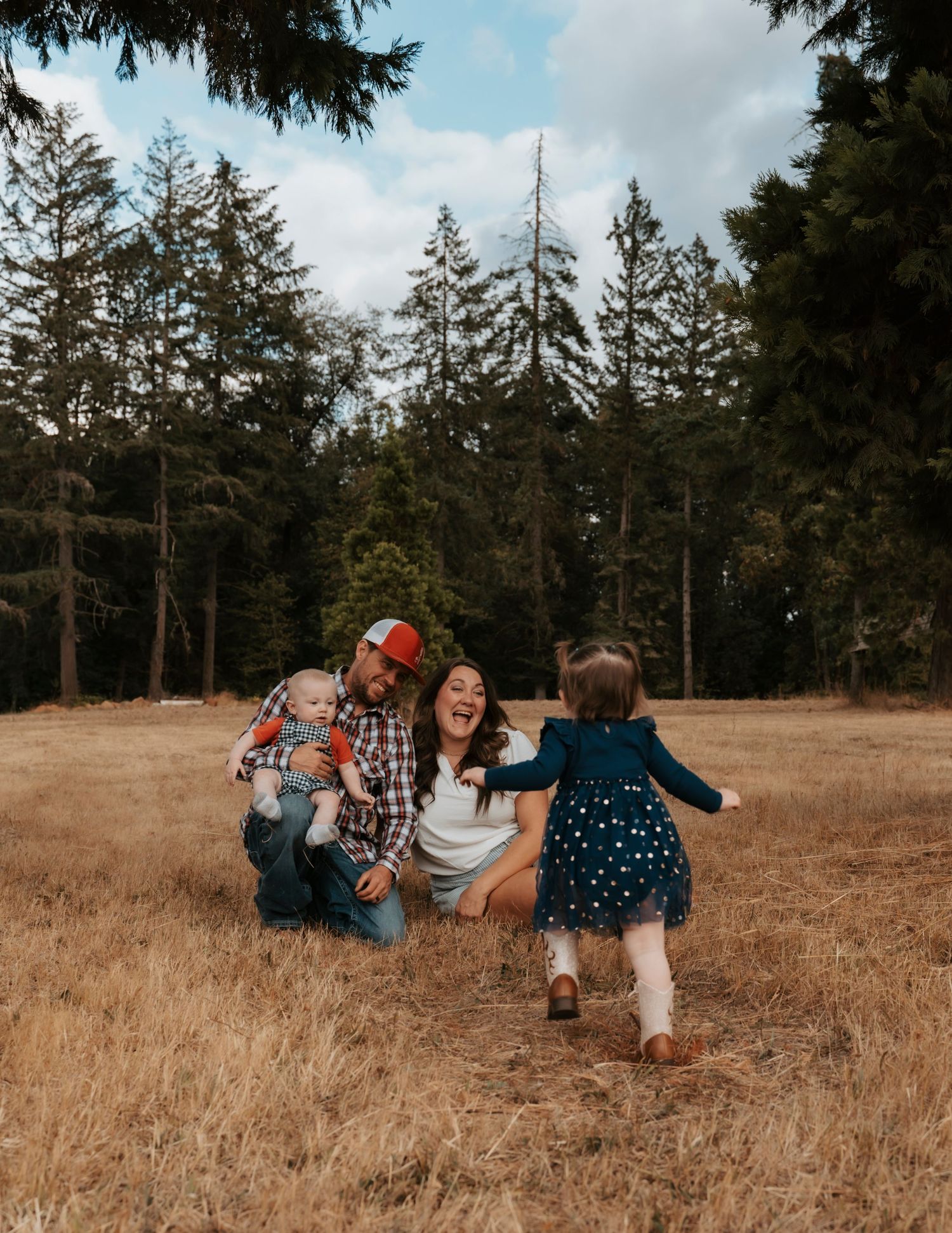 Family playing together in a field with tall evergreen trees in the background.