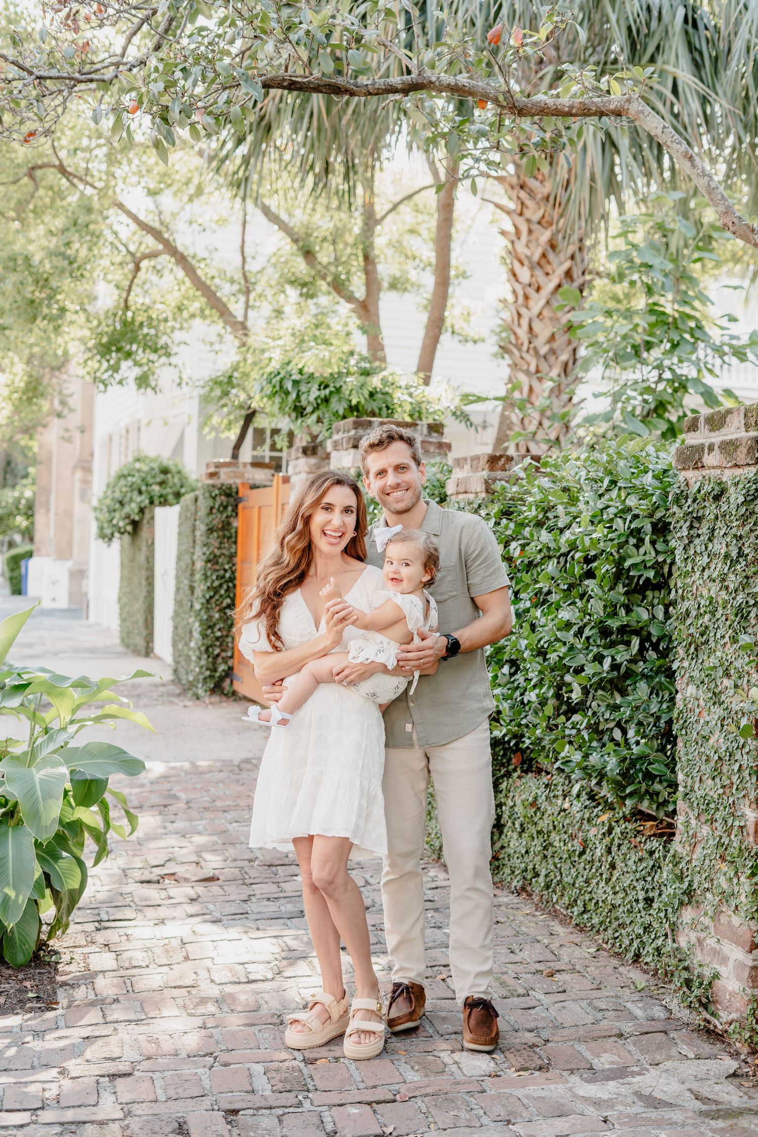 Family portrait on charming cobblestone path lined with lush greenery and palm trees.