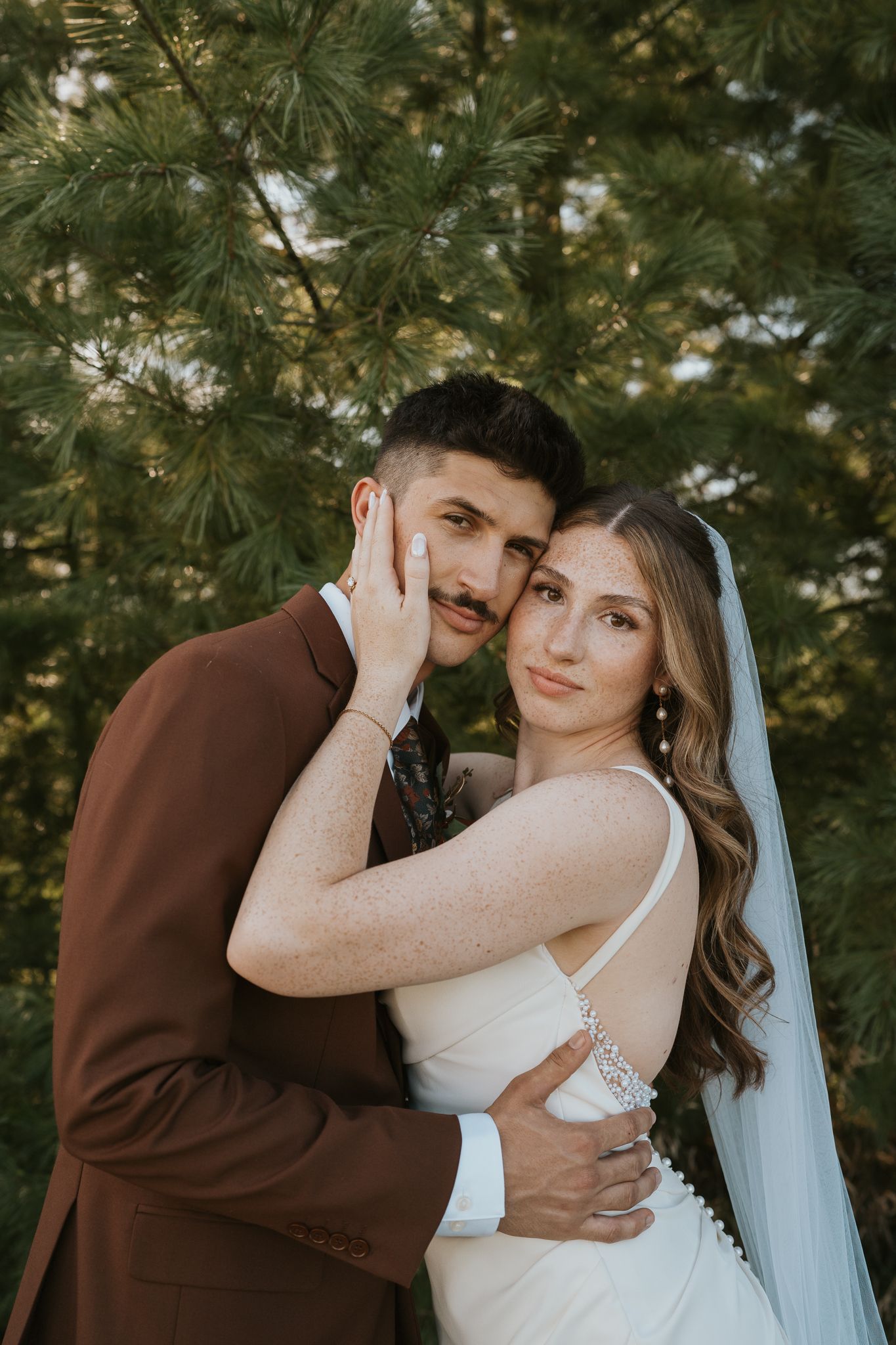 Wedding couple sharing intimate moments against evergreen pine trees in Jackson MI.