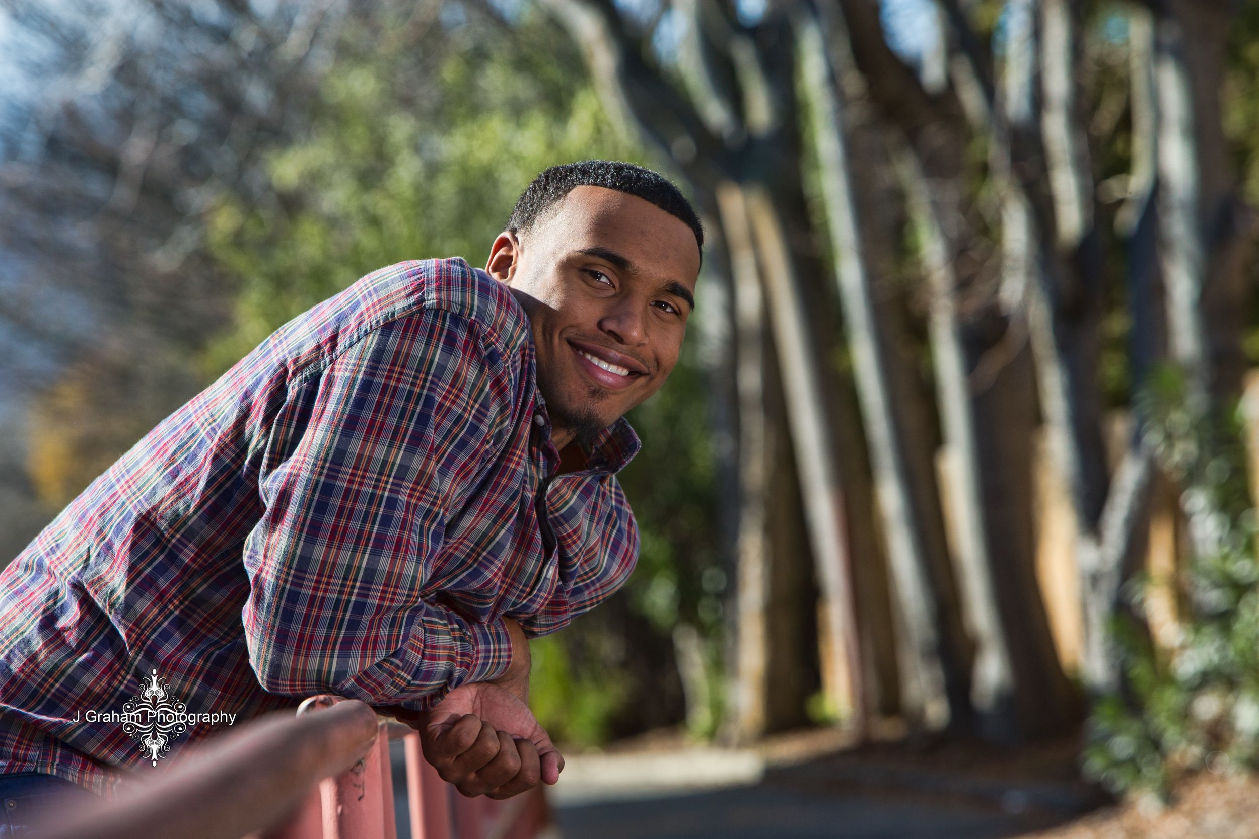 A person in a plaid shirt laughs while walking through a forest path on a sunny day.
