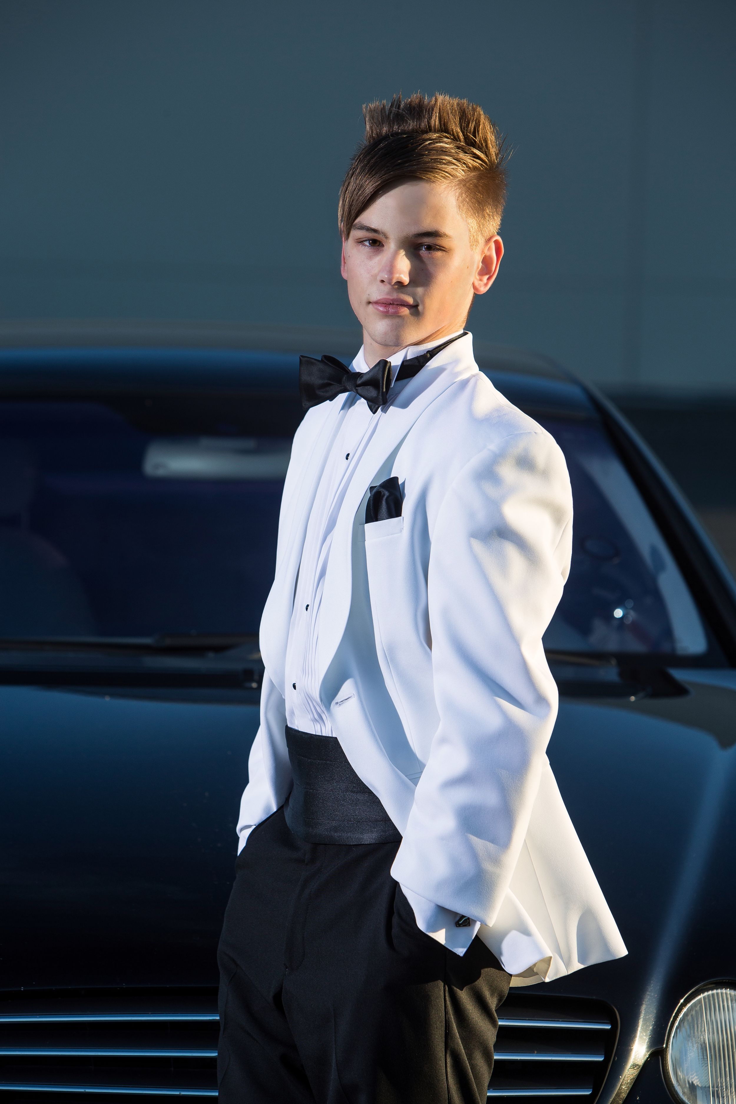 A person in formal attire consisting of a white dress shirt and black vest poses against a dark background.