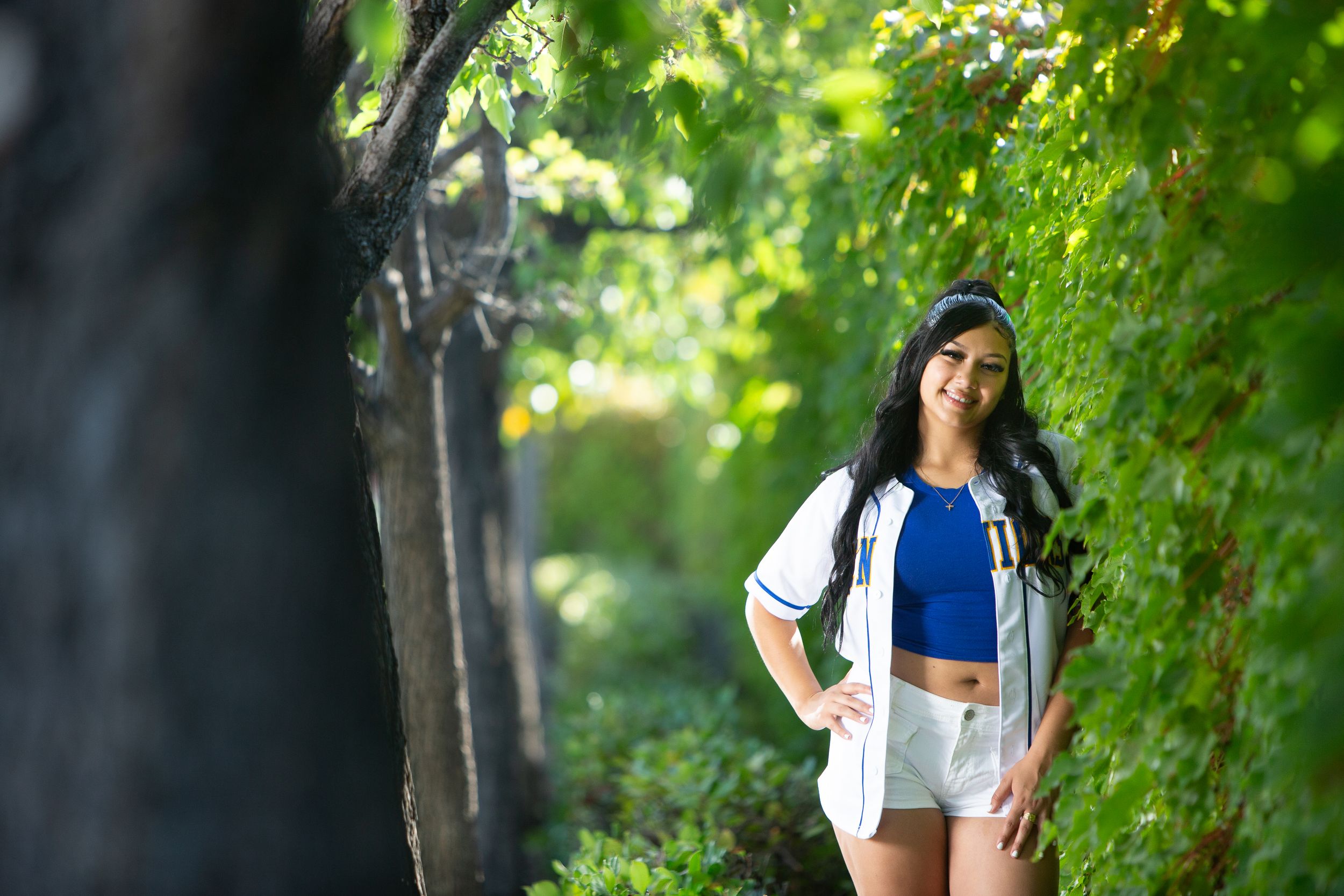Athletic person in workout attire poses confidently in a lush green park setting during a sunny day.