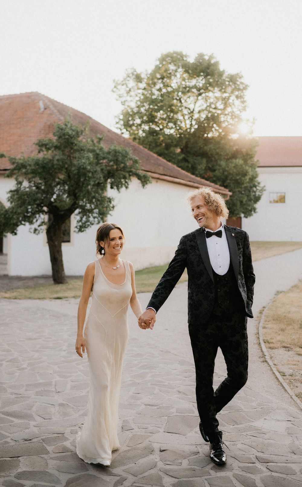 Newlyweds walking hand in hand on stone pathway at historic venue.