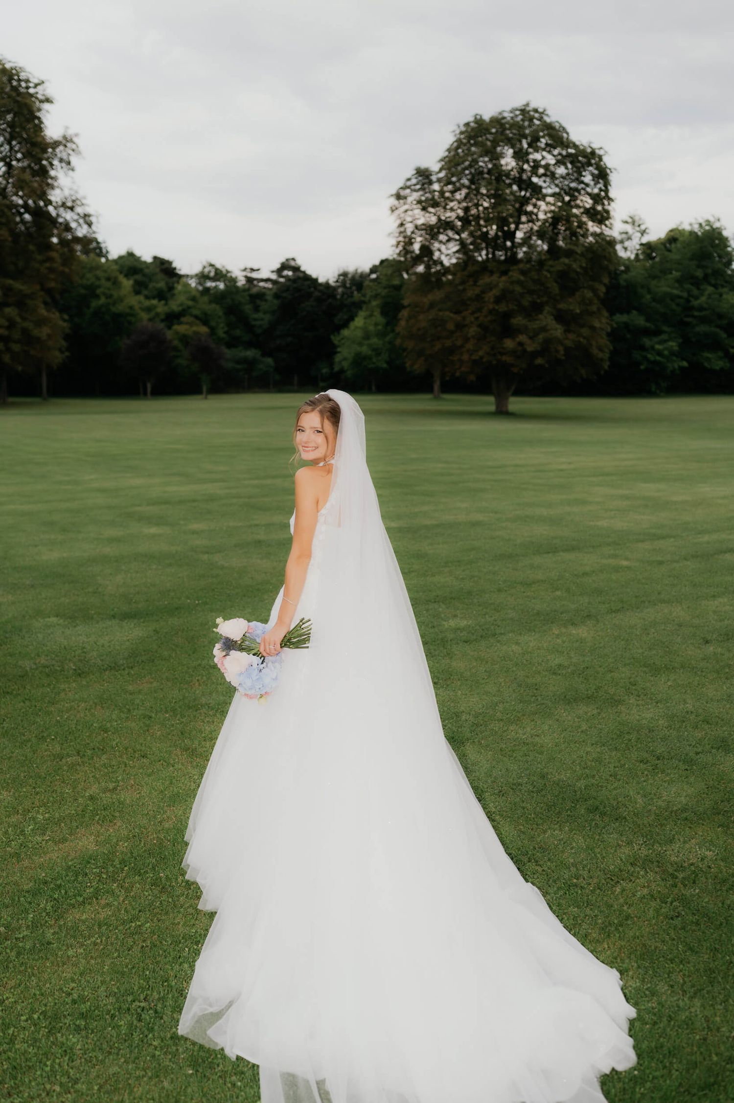 A bride in a flowing white wedding dress walks across a lush green field on her special day.