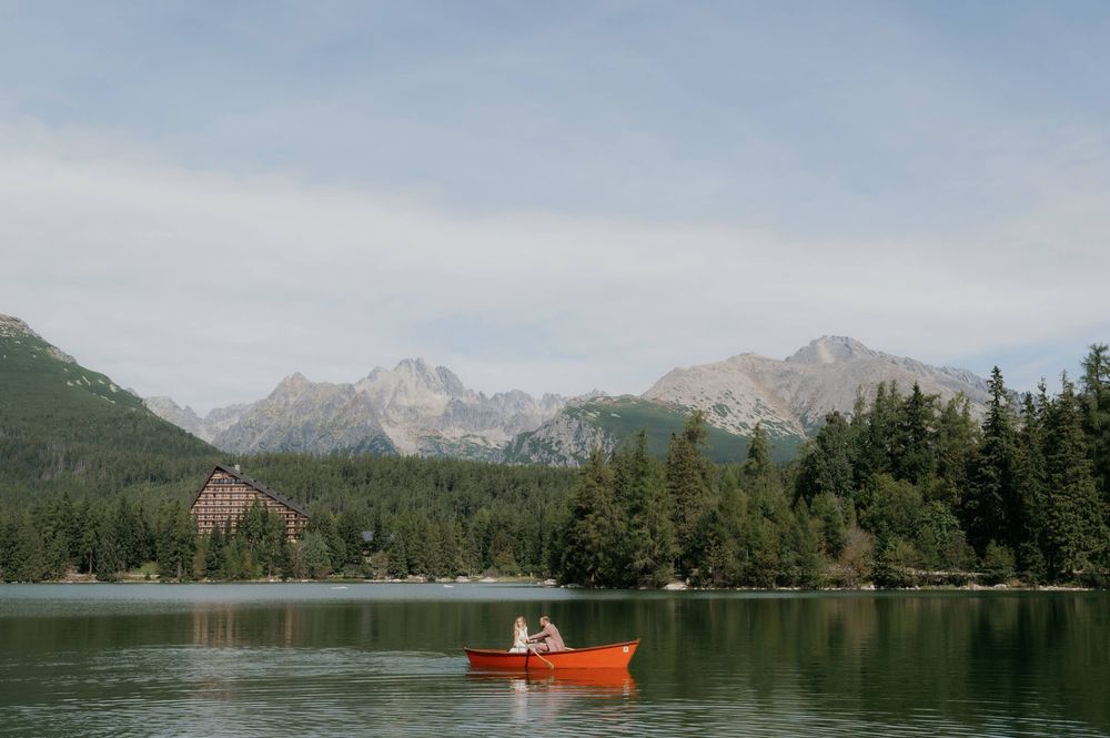A red canoe glides across a serene mountain lake surrounded by evergreen forest and snow-capped peaks.