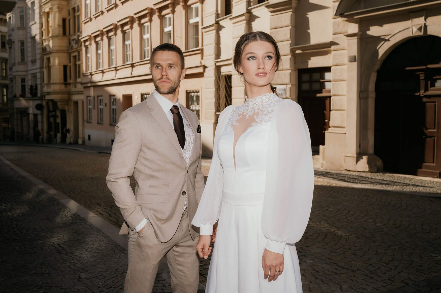 Couple poses on charming cobblestone street wearing formal wedding attire.