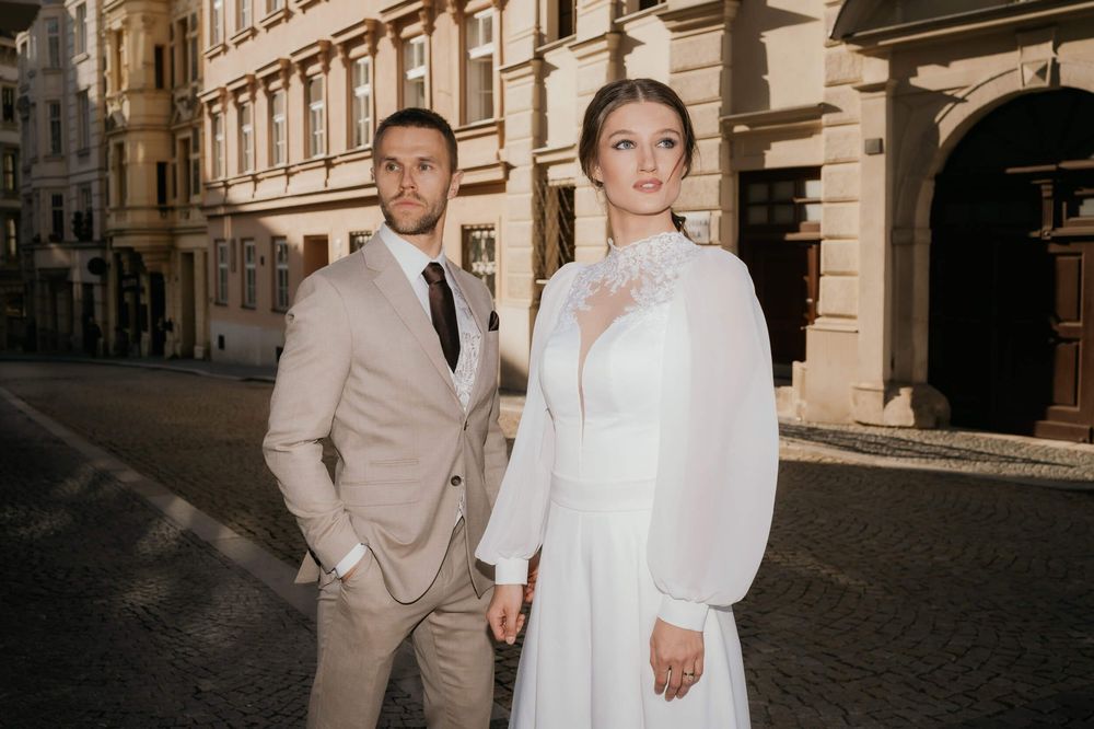 Couple poses on charming cobblestone street wearing formal wedding attire.