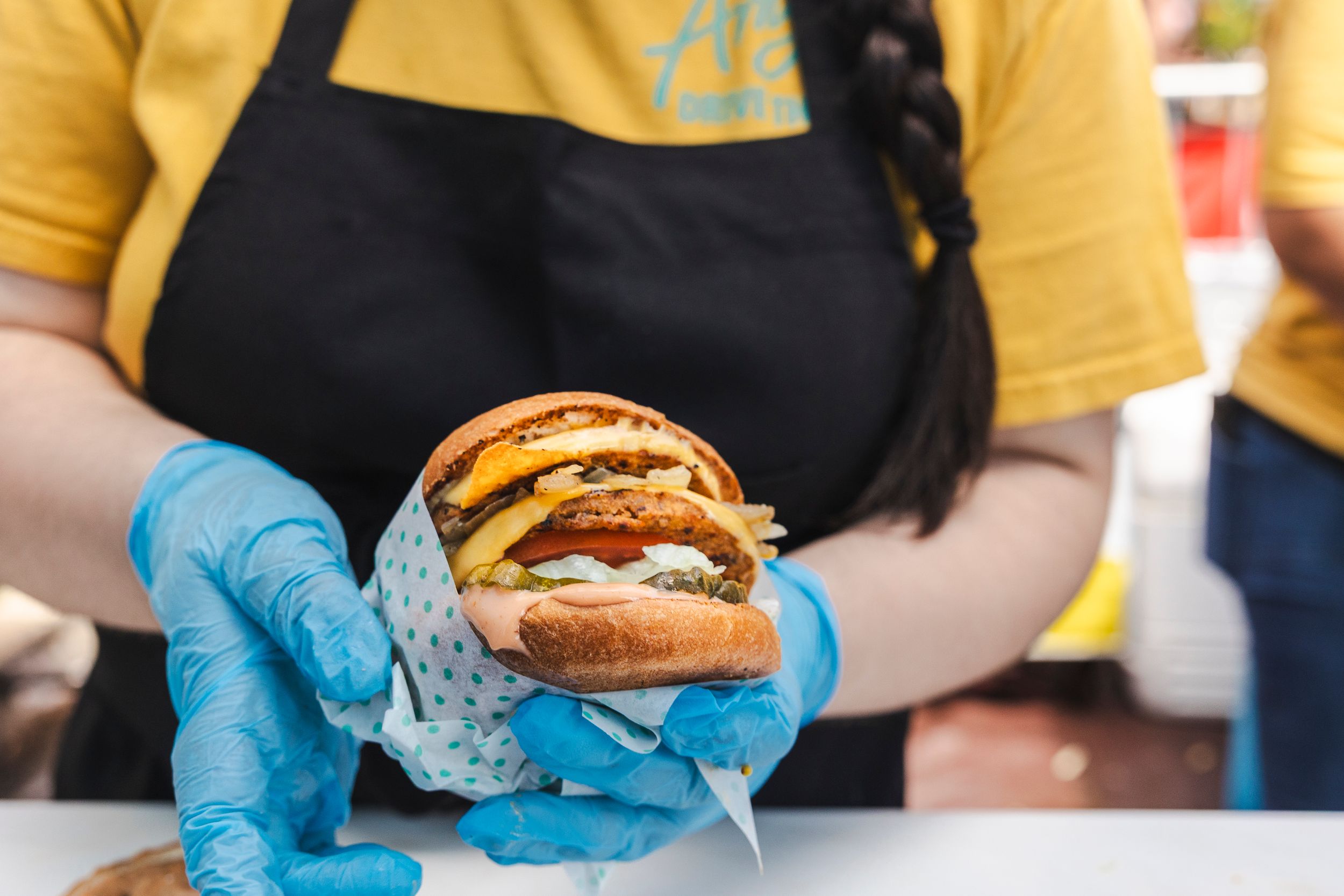 Hands wearing blue gloves preparing sandwiches at an outdoor food service station.