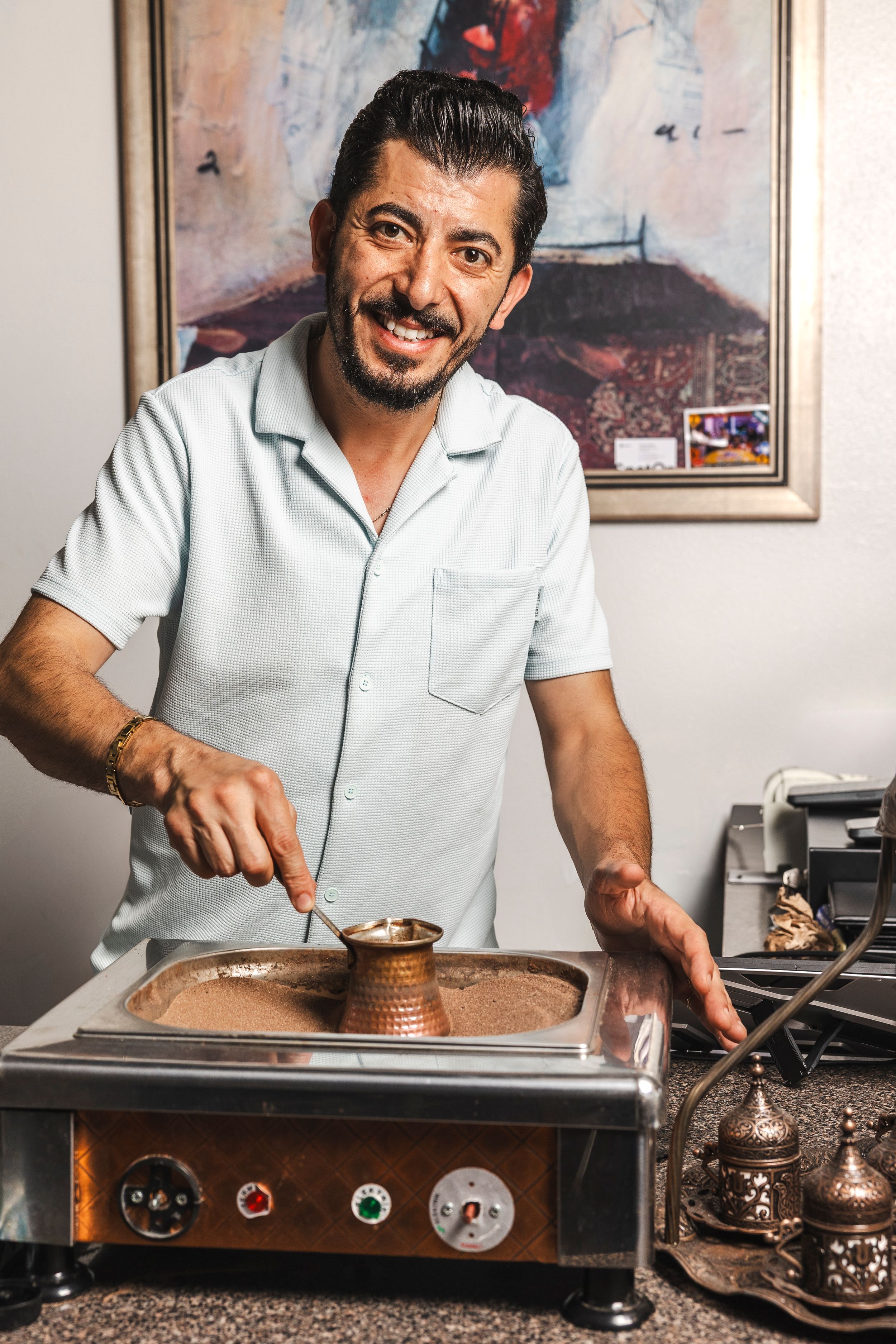 Person in white polo shirt preparing traditional Turkish coffee using copper cezve pot on wooden surface.