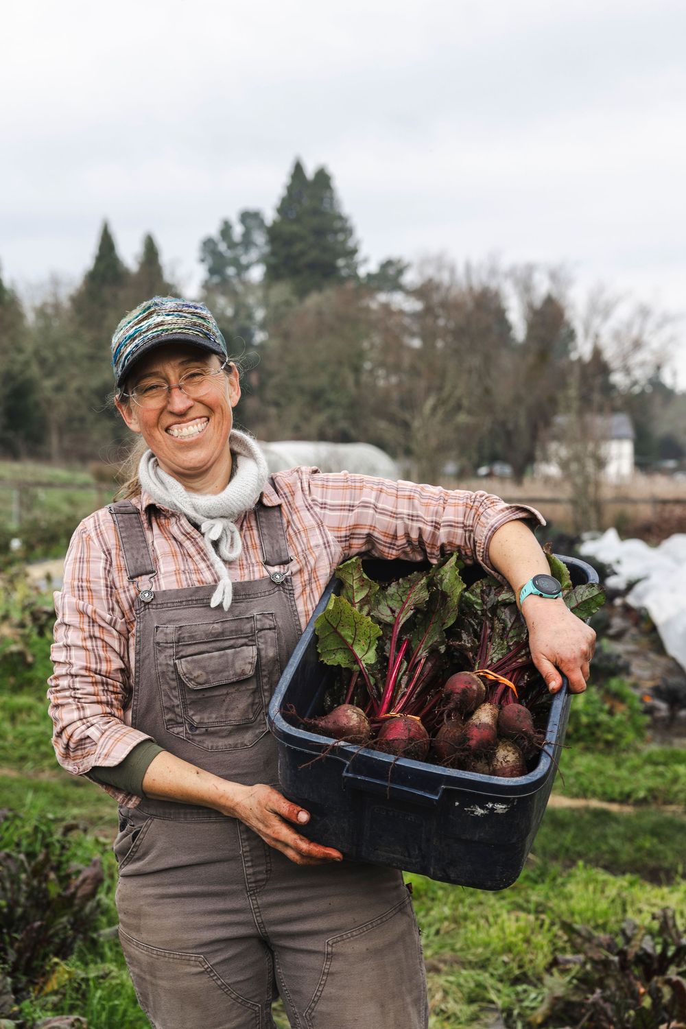 A gardener in overalls and plaid shirt proudly displays freshly harvested beets from a community garden.