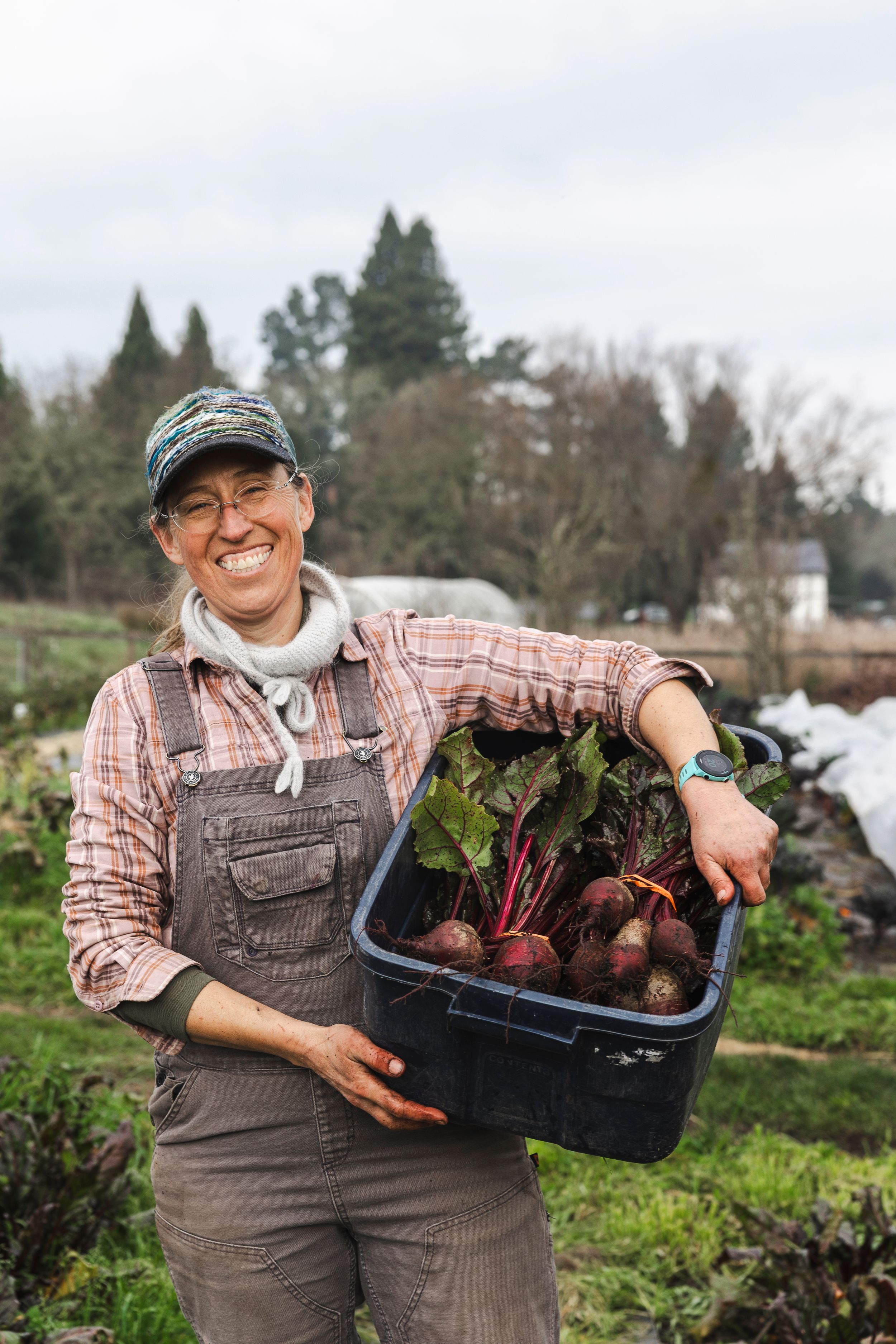 A gardener in overalls and plaid shirt proudly displays freshly harvested beets from a community garden.