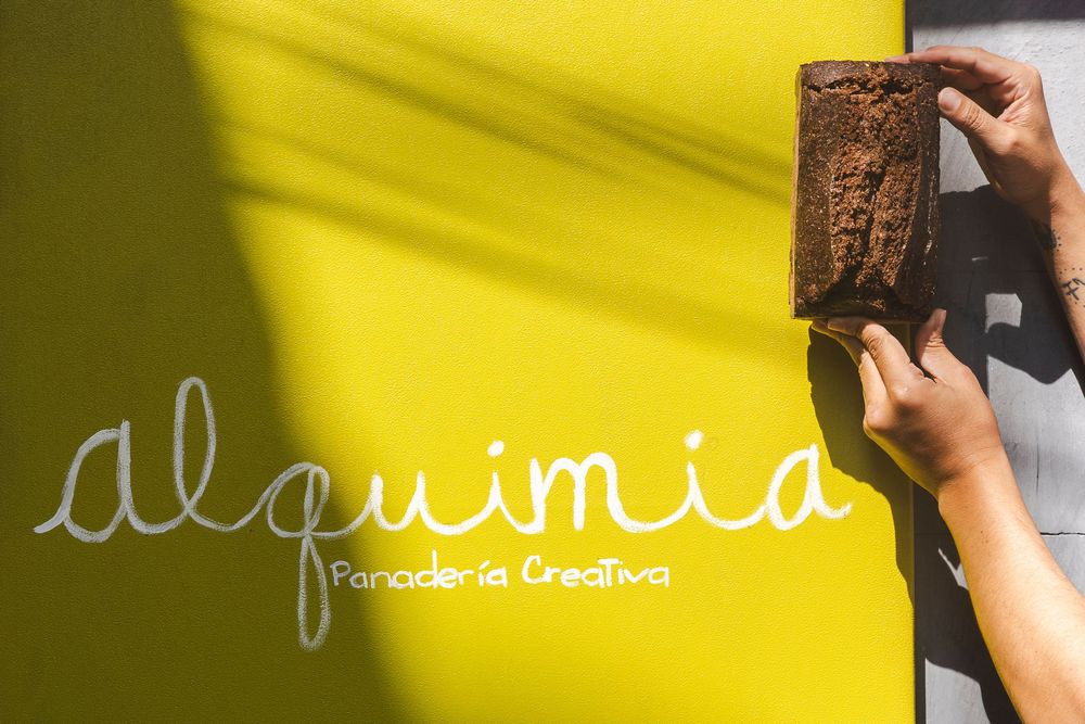 Hand holds up a wooden block against a bright yellow background with blurred text visible.