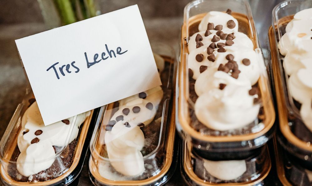 Tres Leche desserts topped with whipped cream and chocolate chips in individual containers.