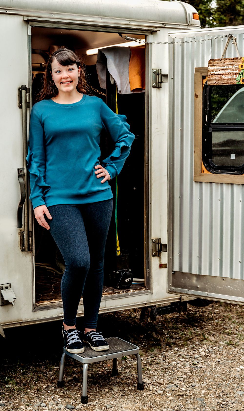 A casual pose in front of a white mobile trailer while wearing a teal sweater and jeans.
