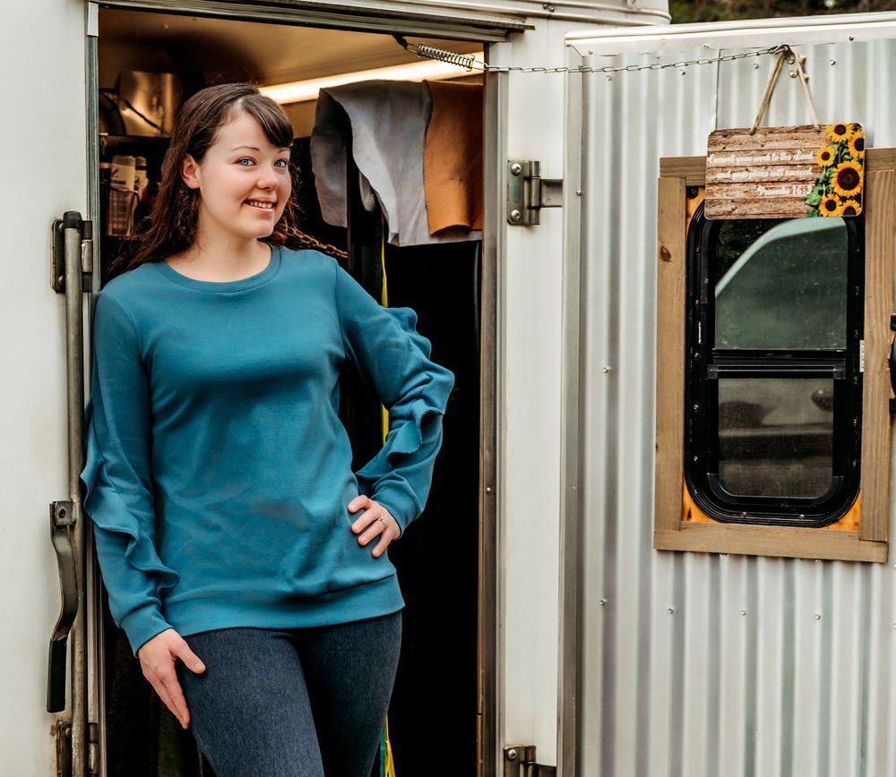 A person in a teal sweater stands in the doorway of a white mobile trailer.