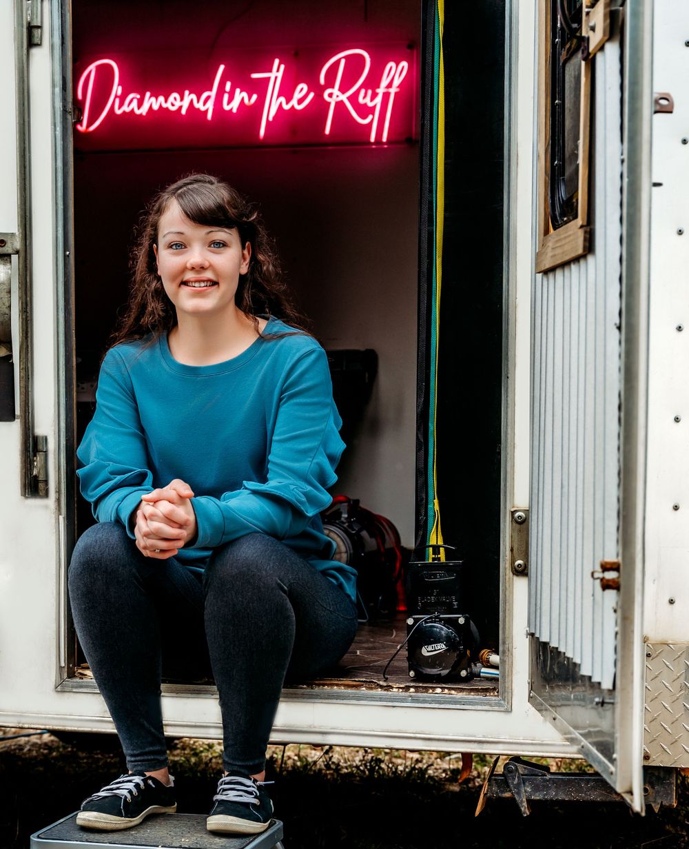 A casual pose under a pink neon sign reading 'Diamond in the Ruff' inside a white trailer.