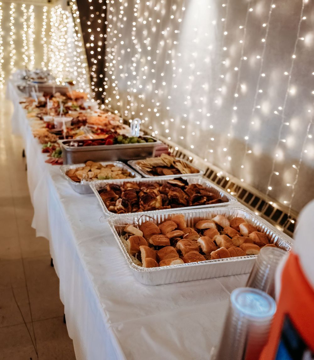 A wedding buffet table with twinkle lights featuring multiple chafing dishes of food.