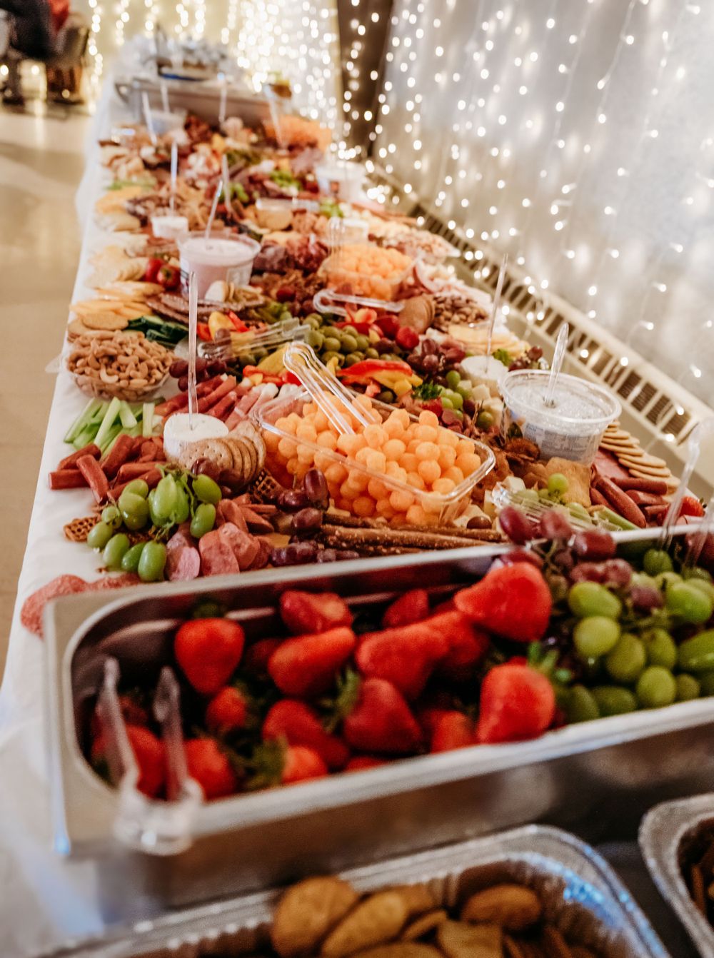 An elegant grazing table with fresh fruits, meats, and cheeses illuminated by string lights.