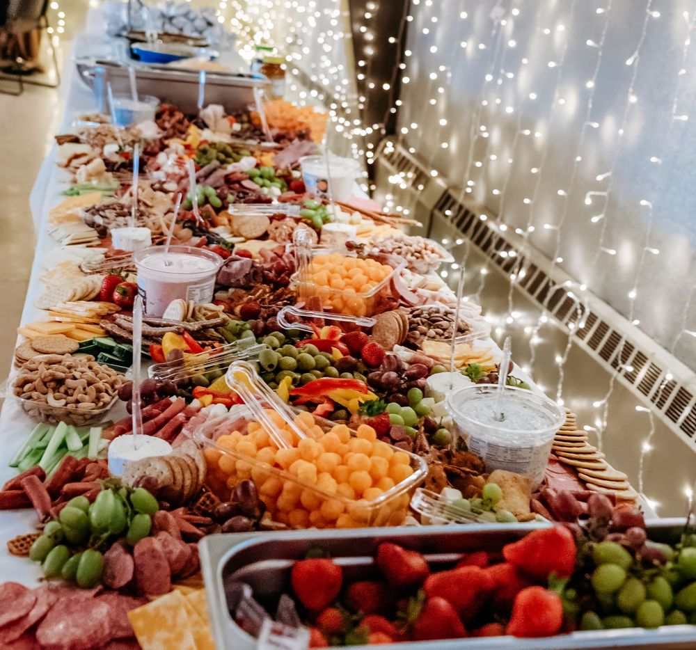 A lavish buffet spread with charcuterie, fresh fruits, and appetizers under twinkling fairy lights.