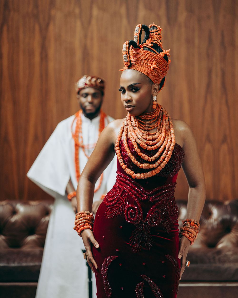 Traditional Nigerian wedding attire featuring rich burgundy dress and ornate coral beaded jewelry in cultural ceremony.