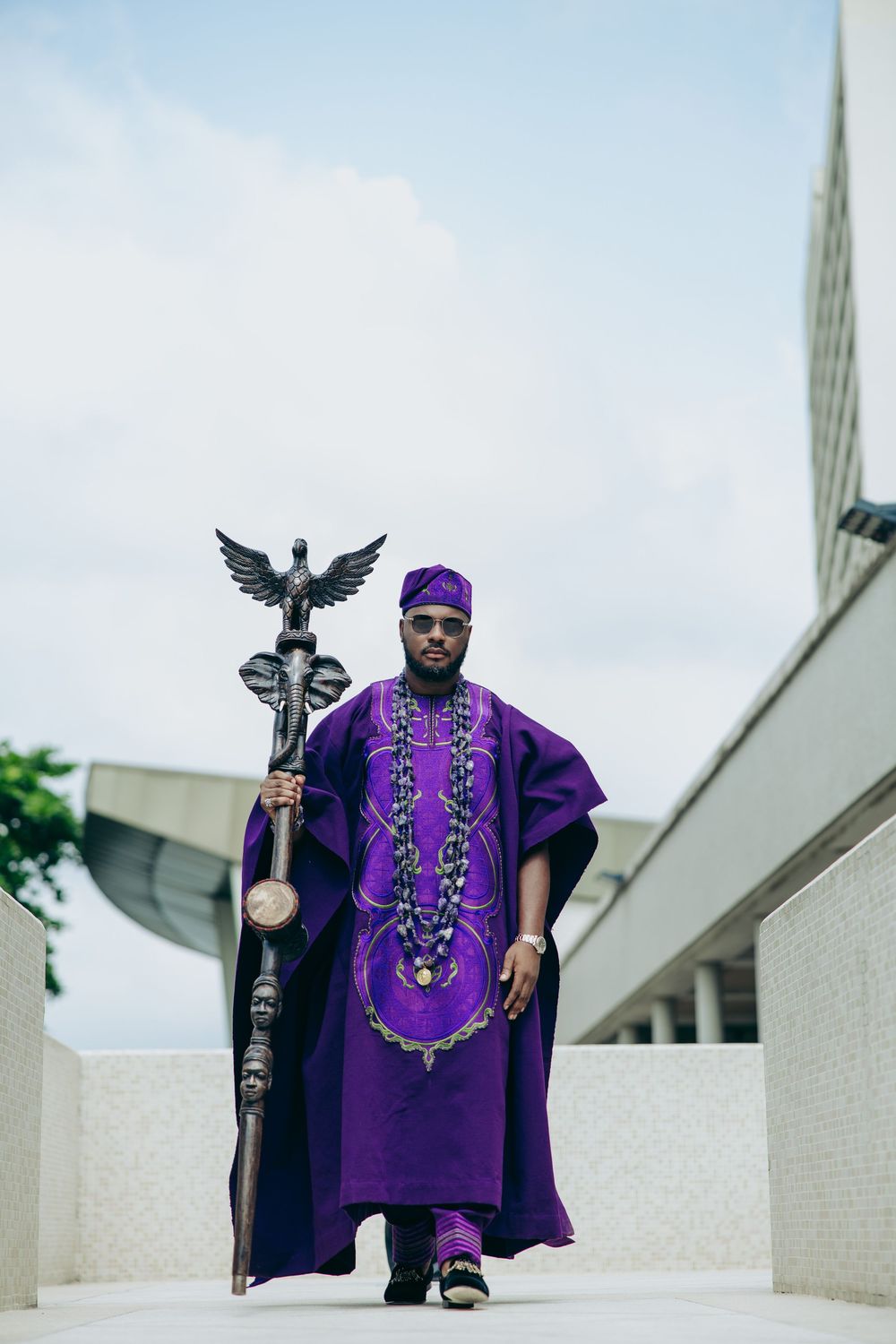 Traditional African formal wear featuring a purple agbada with ornate embellishments and ceremonial staff.