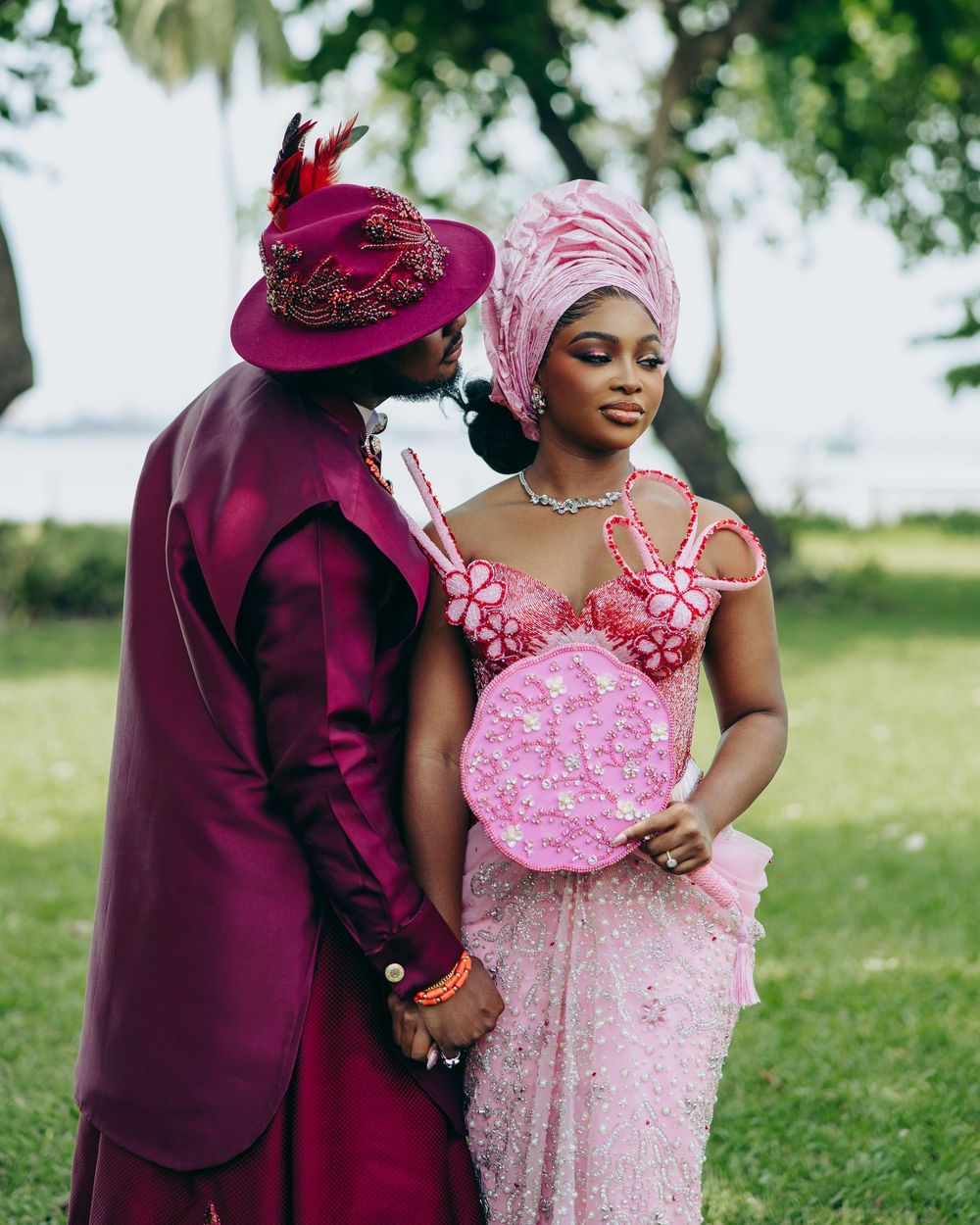Couple in burgundy and pink formal attire embracing outdoors in a romantic photoshoot.