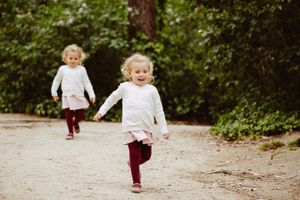 Children run playfully along a dirt path surrounded by lush greenery.