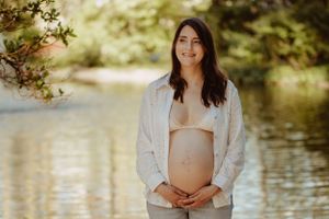 Woman in white dress poses by a serene pond with natural lighting.