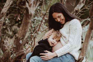 Joyful maternity photo showing a pregnant woman and child laughing together outdoors.