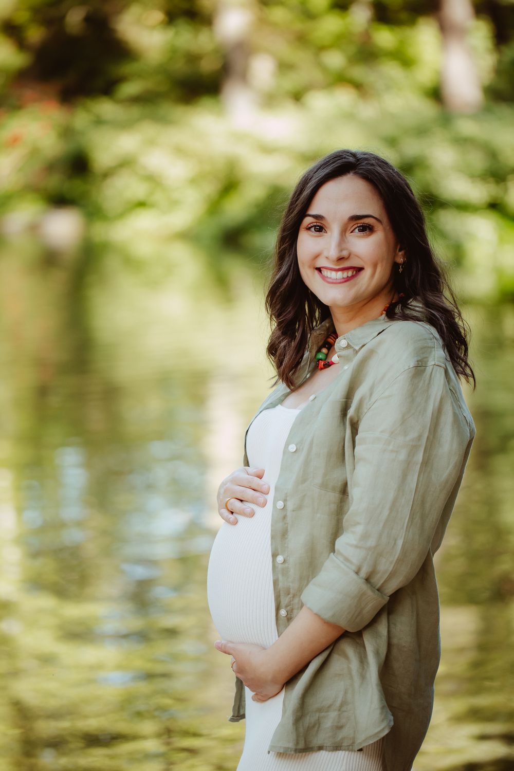 Maternity photoshoot in nature with soft green reflections on water.