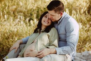 Couple embracing during sunset maternity photo session in golden field.