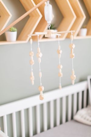 Neutral colored wooden mobile hanging above white crib with geometric wall decor during a lifestyle session in Springfield, Missouri.