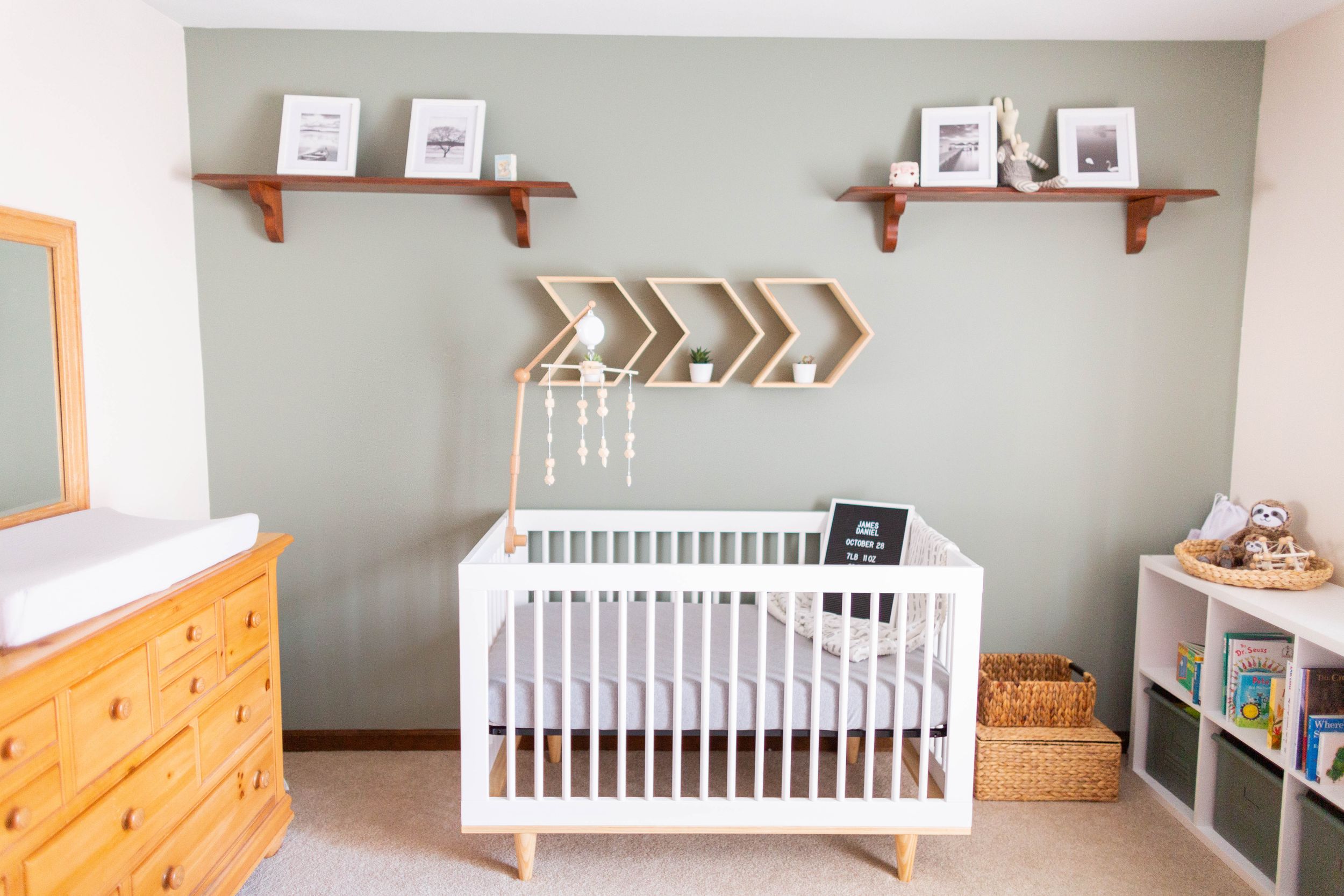 Modern nursery with white crib, wooden chevron wall art, and floating shelves taken during a lifestyle session in Springfield, Missouri.