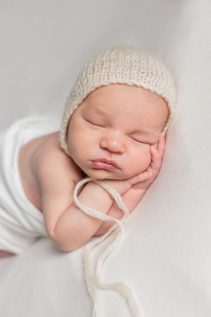 Sleeping newborn in cream knit bonnet on white backdrop taken during a lifestyle session in Springfield, Missouri.