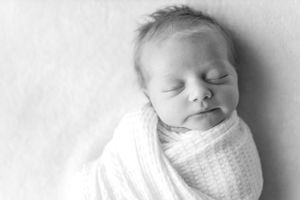 Black and white portrait of peaceful sleeping newborn wrapped in white swaddle during a lifestyle session in Springfield, Missouri.