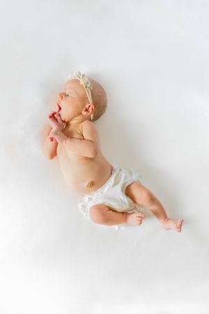 Newborn baby wearing white diaper and headband lying on white background during a lifestyle session in Springfield, Missouri.