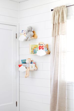 White nursery wall with floating cloud shelves displaying children's books during a lifestyle session in Springfield, Missouri.