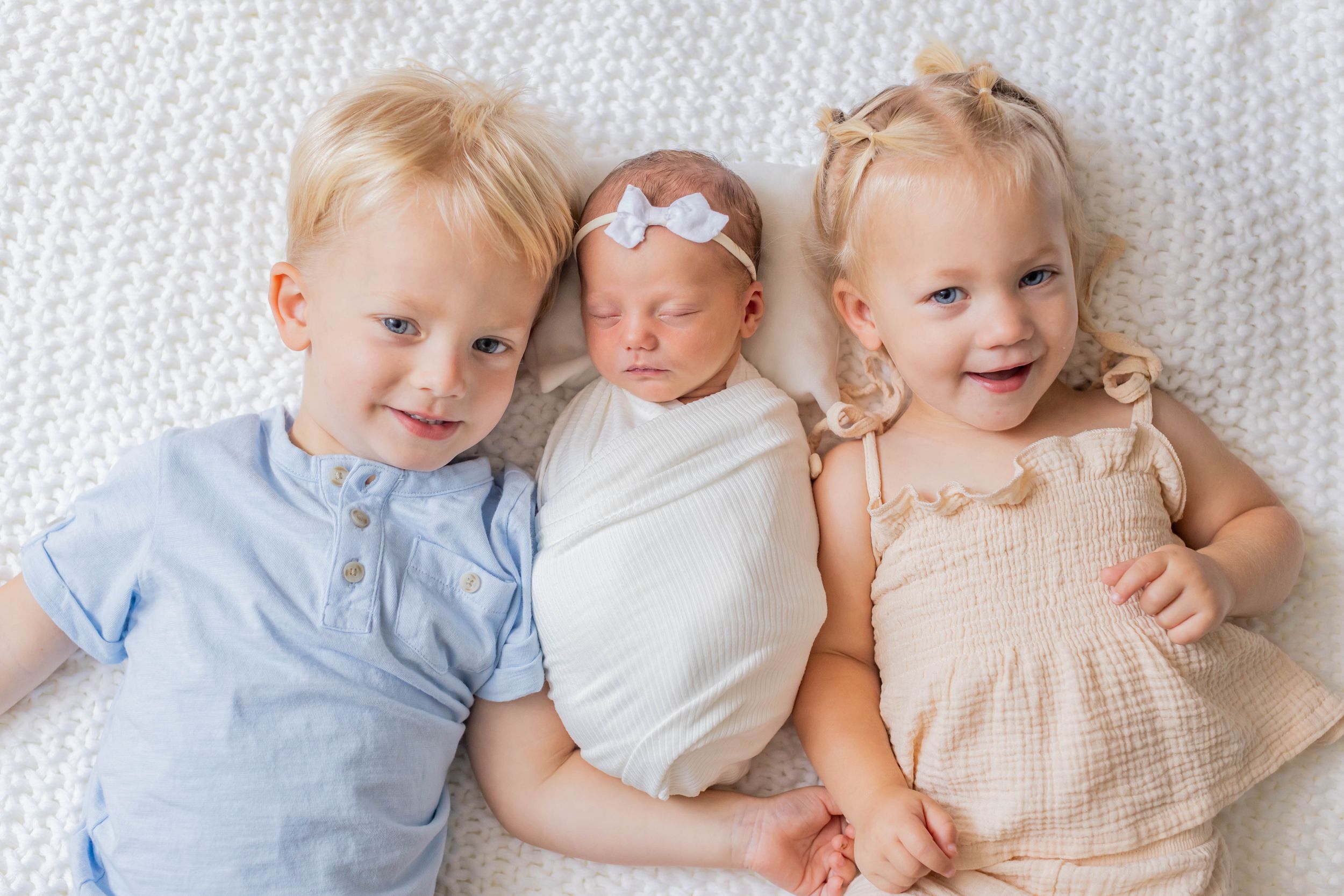 Three young children cuddling together on white knit blanket during a lifestyle session in Springfield, Missouri.
